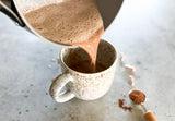 hormone health hot cacao in a mug with cinnamon and foam on top, happy cacao evening drink with hormone health capsules opened on the table, plant based hormone support evening ritual warm drink