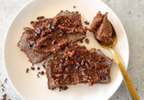 Healthy chocolate hazelnut toast on sourdough bread with Happy Cacao spread, Closeup of chocolate hazelnut spread on toast, Happy Cacao superfood powder jar with hazelnut butter, Healthy Nutella toast recipe flat lay