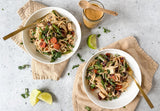 green peanut noodle bowl with golden tofu stir fried vegetables and cilantro, soba noodles with creamy peanut sauce and daily greens, plant based peanut noodle bowl topped with sesame seeds and lime, healthy stir fry noodle bowl with sriracha peanut sauce