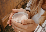 Happy Cacao powder with spoon and plant milk, Frothed chocolate latte with Happy Cacao superfood powder, Healthy hot chocolate latte with collagen support, Kristel holding cacao latte morning ritual