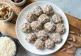 hormone health bliss balls on a plate dusted in shredded coconut, no bake hormone support energy balls with maca shatavari ayurvedic herbs, cashew date bliss balls with hormone health capsules opened, healthy women's hormone balance snack balls